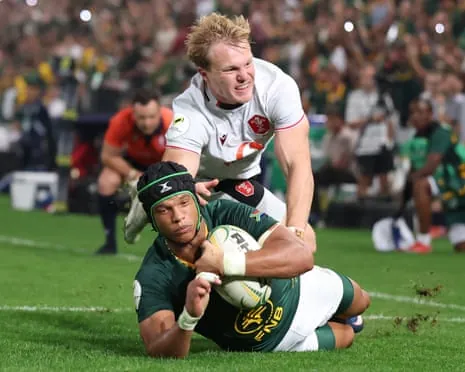 Kurt-Lee Arendse in green slides on the ground holding the ball while being tackled by a player in white